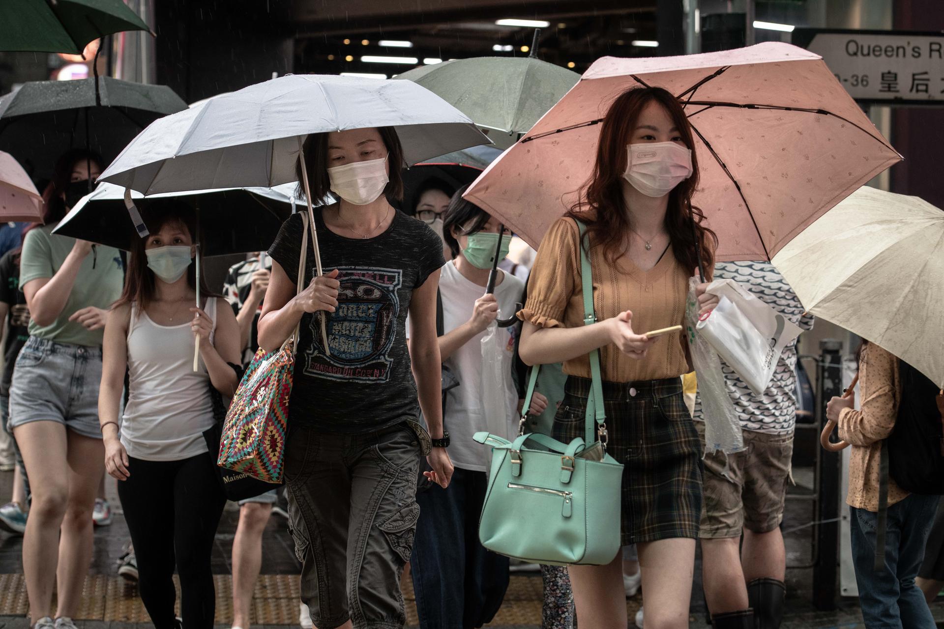 Pedestrians wearing protective masks take shelter under umbrellas while crossing a street in the Central district in Hong Kong, China. An overwhelming majority of Hong Kong residents said they oppose a controversial new security legislation that China plans to impose on the city, a move that has generated criticism from western democracies amid concerns over basic freedoms in the financial hub. Bloomberg