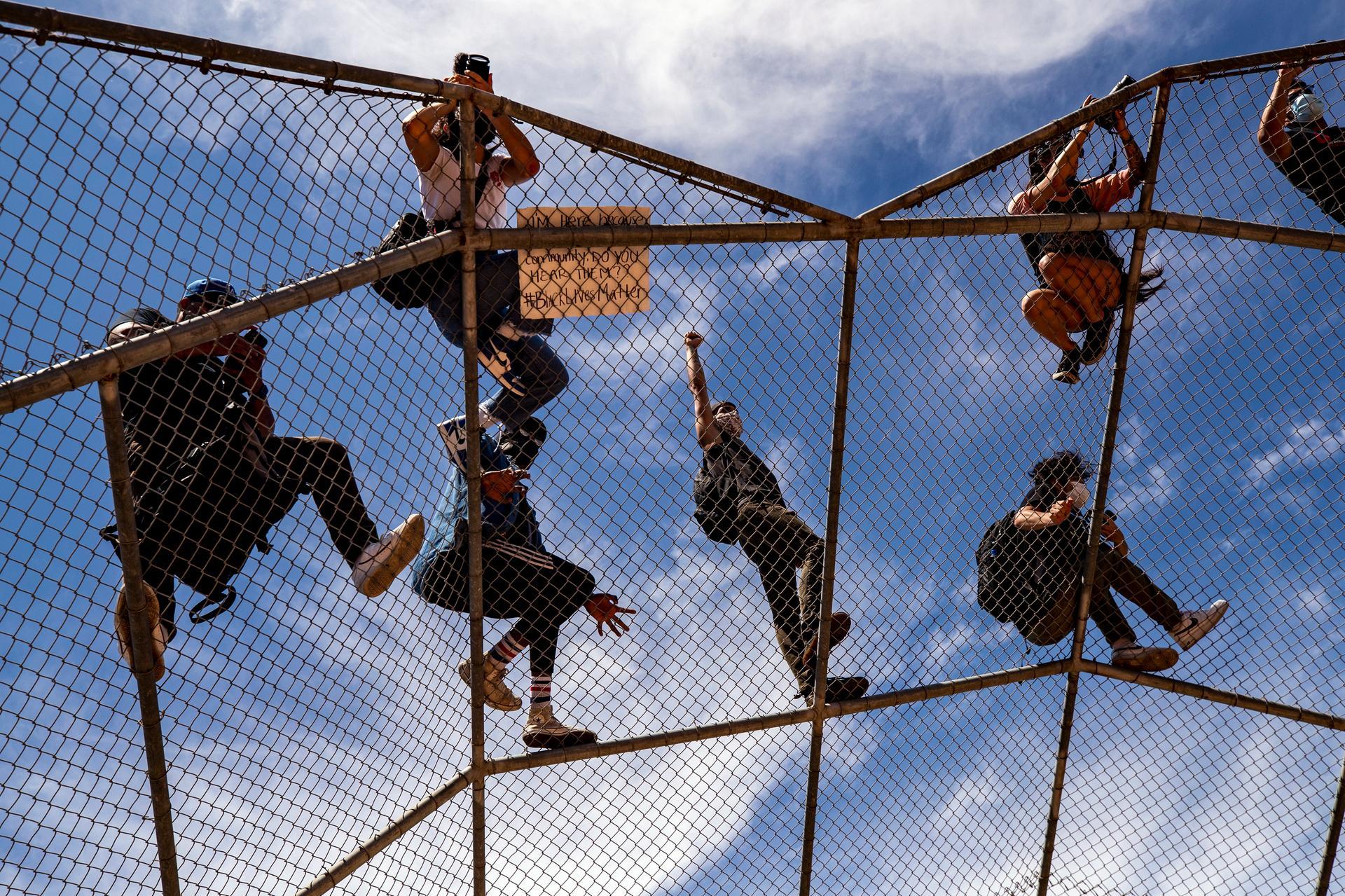A protester raises his fist in reaction as he and others stand on an overhanging fence as thousands of protesters gather at the Pan Pacific Park to demonstrate following the death of George Floyd, in Los Angeles. EPA